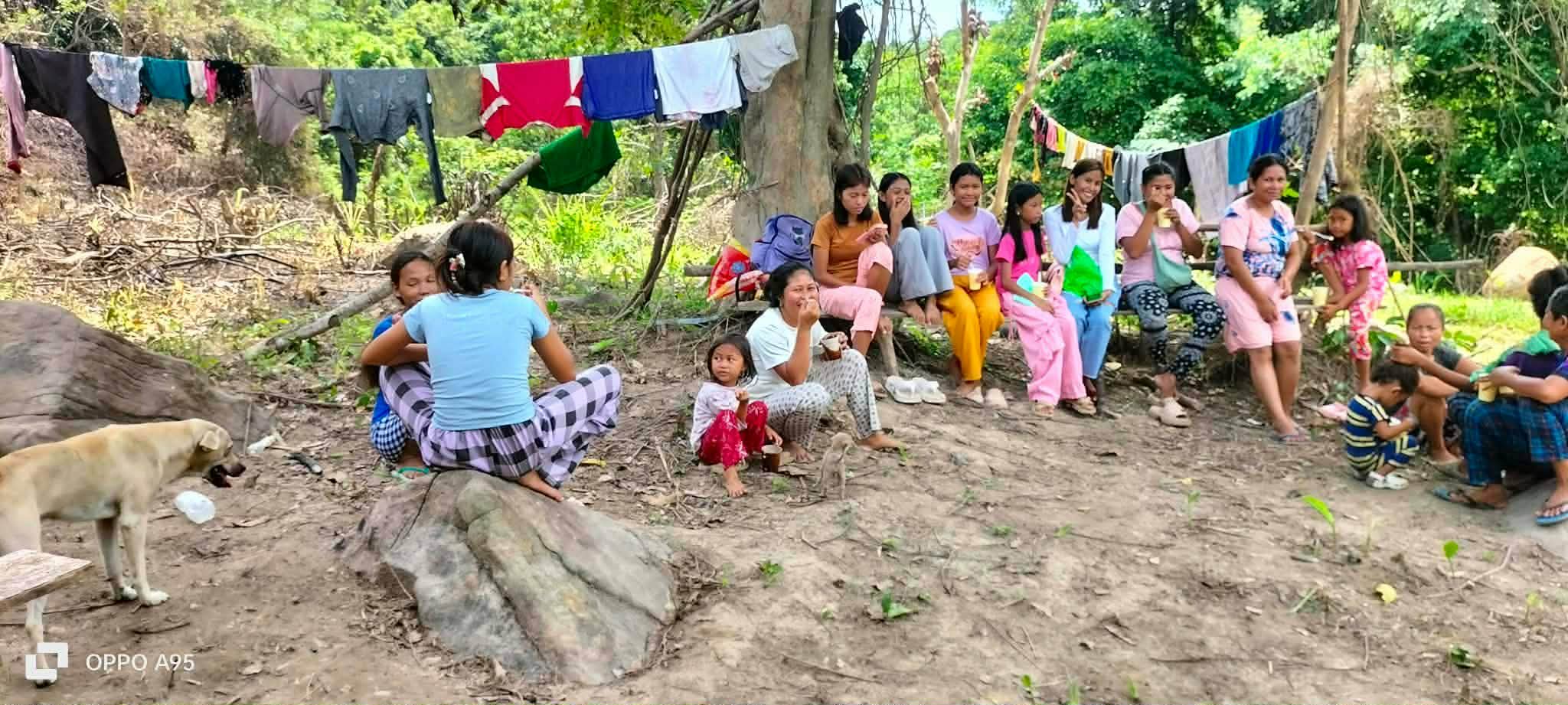 Women and children gathered outdoors near homes and a clothesline
